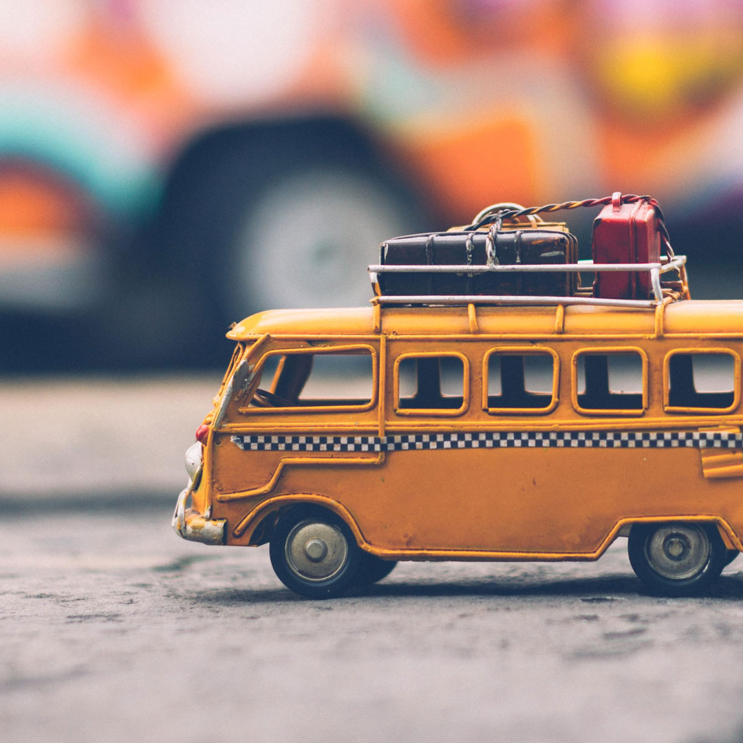 Toy bus with luggage on top sits on a table with blurred background of the big world behind it.